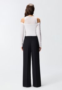 Witte lange mouwtop met een off-shoulder ontwerp, gecombineerd met hoge zwarte wijde broekspijpen. Glad textuur en een op maat gemaakte pasvorm zijn duidelijk aanwezig.