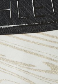 White fabric featuring metallic gold abstract lines, with a textured black band displaying embossed lettering.