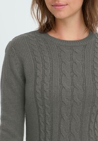 Gray cable-knit sweater featuring a round neckline, textured patterns, and ribbed cuffs, highlighting a soft and cozy appearance.