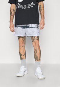 Sort grafisk t-shirt med hvid tekst, mesh grå shorts med et mønster, og hvide sportsko med grå sokker.