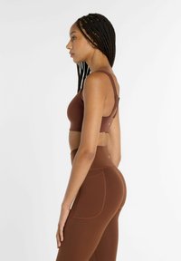 Brunt sport-bh- och leggingsset med en figurnära design, slät textur och justerbara axelband, samt en sidoficka på leggingsen.