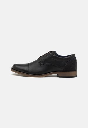 Chaussure de ville en cuir noir avec une finition lisse, bout rond, semelle brune contrastante, et un mélange d'accents en daim sur le talon et le dessus.