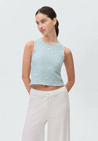 Svetlo modrý skrátený top s textúrovanou látkou, okrúhlym výstrihom a volánovým lemom. Skombinovaný s bielymi nohavicami na šnúrku.