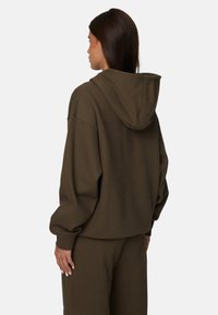 Brązowa bluza z kapturem o luźnym kroju, ze opadającymi ramionami i ściągaczami u rękawów. Miękka tekstura, materiał o średniej wadze.