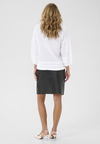 Top bianco con texture e maniche tre quarti, abbinato a una gonna a matita in pelle nera. Tacchi a spillo completano l'outfit.