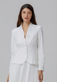 Blazer blanc à coupe ajustée, col cranté et fermeture à cinq boutons. Texture lisse avec des détails subtils le long des coutures.