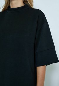 Zwart gestructureerd top met een hoge, ronde halslijn en korte, brede mouwen. Zachte stof met een gladde textuur en minimale details.