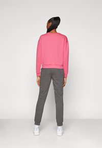 Rosa hettegenser og grå joggebukser, med en avslappet passform, ribbede mansjetter, glatt tekstur, og sammen med hvite sneakers.
