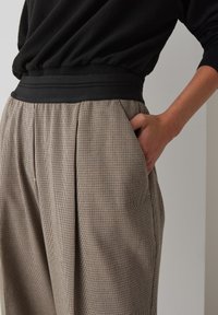 Hosen mit einem schwarzen elastischen Bund und einem strukturierten, karierter Muster in Beige und Braun. Verfügt über Seitentaschen und Falten.