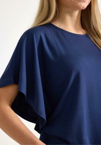 Mörkblå topp i mjukt tyg med lös passform, har vida ärmar och rund halsringning, och visar en minimalistisk design.