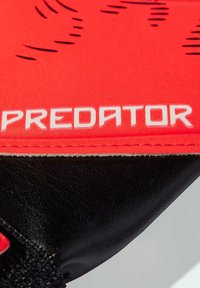 Rode en zwarte sporthandschoen met een gestructureerd stoffen oppervlak, met het woord "PREDATOR" in vetgedrukte witte letters op het rode gedeelte.