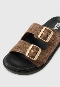 Brune slidesandal med to brede stropper med guldspænder, vævet tekstur på overdelen og en sort sål. Glat overflade med minimalistisk design.