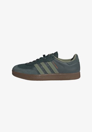 Dunkelgrüner Adidas Velosamba Sneaker mit Wildleder-Zehenkappe, drei hellgrünen Streifen, brauner Sohle und Schnürverschluss, von der Seite gezeigt.