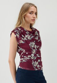 Top senza maniche floreale con scollatura drappeggiata, tessuto borgogna e motivo floreale bianco; presenta dettagli arricciati lungo i lati.