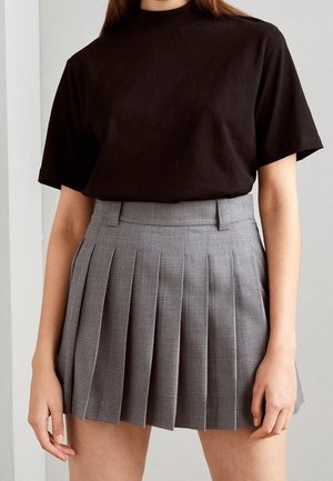 Personne portant un haut noir à manches courtes rentré dans une mini-jupe plissée taille haute gris à motif à carreaux subtil.