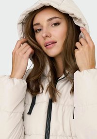 Hellbeige gefütterte Jacke mit Kapuze, schwarzen Akzenten und einem durchgehenden Reißverschluss. Verfügt über eine gestepptes Muster und ein weiches Obermaterial.