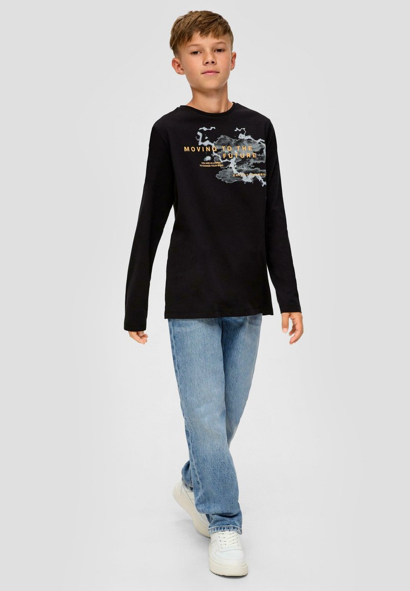 T-shirt noir à manches longues avec impression graphique et texte doré, associé à un jean droit bleu clair et des baskets blanches. Modèle présenté par un enfant.