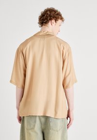 Korte mauve shirt met een ontspannen pasvorm, rug yoke en zachte textuur. Gecombineerd met lichtgroene denim broek met achterzakken.
