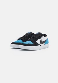 Tenisky Nike s černým semišovým svrškem, modrými semišovými akcenty, bílou stélkou a černým logem. Zavazování na tkaničky s texturovanými detaily.