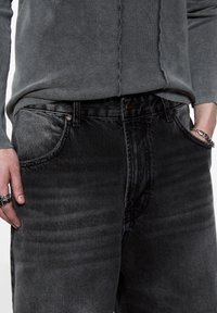 Jean en denim noir avec une texture délavée, design à cinq poches et coutures renforcées au niveau des coutures. Fermeture par bouton métal et zipper.
