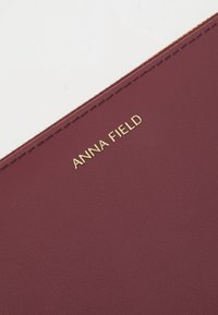 Burgundy faux leather notebook cover with gold embossed "ANNA FIELD" text. Smooth texture, minimalistic design, clean edges.