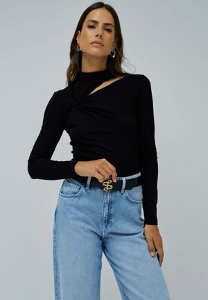 Top negro de manga larga con un detalle retorcido en un hombro, combinado con jeans de mezclilla azul de tiro alto y un cinturón negro con hebilla dorada.