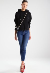Sudadera negra corta con cordones, combinada con jeans ajustados azules. Zapatos de tacón rojos y un pequeño bolso cruzado negro con embellishments.