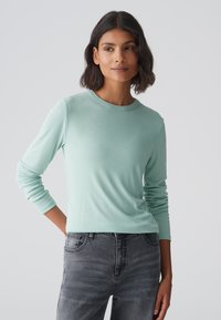 Licht mintgroen langemouwen shirt met een ronde hals, gemaakt van zachte stof. Gecombineerd met grijze jeans met vijf zakken.