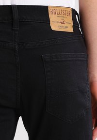 Svarta denimjeans med en åtsittande design, med en framträdande läderetikett i tan på midjan och en bakficka med diskret sömnad.