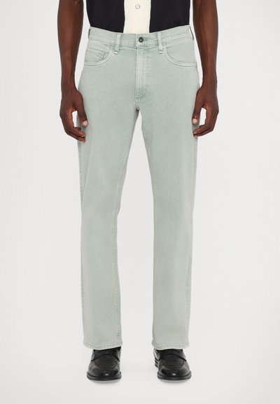 Helle grüne Denim-Jeans mit geradem Bein, Five-Pocket-Design und einer subtilen Textur. Getragen mit schwarzen Schuhen und einem mehrfarbigen Hemd.
