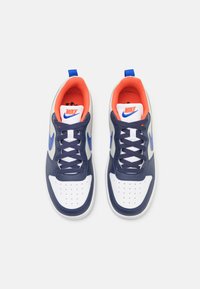 White and navy leather sneakers featuring a perforated toe, blue swoosh logo, orange accents, and round laces with a blue heel tab.