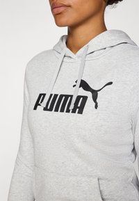 Pelēks kapučjak, kas izgatavots no mīkstas auduma, ir ar lielu melnu "PUMA" logotipu un mazu melnu puma siluetu. Tam ir kangaro kabata un auklas.