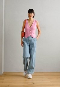 Pink knitted vest with buttons, paired with light blue high-waisted wide-leg jeans, and white sneakers. Holds a small orange handbag.