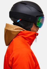 Sort skihjelm med grøn spejlvisir, kombineret med en orange jakke med en beige, tekstureret krave. Logoer synlige på både hjelm og jakke.