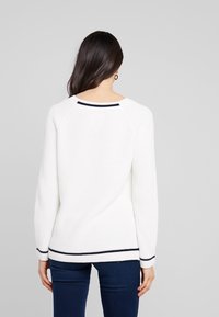 Pull en maille blanche avec une texture côtelée, accents de rayures bleu marine au niveau de l'encolure et des poignets, et une coupe décontractée. Vue de dos avec manches longues.