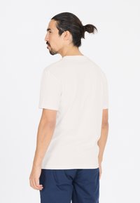 Vaalean beige lyhythihainen t-paita, jossa on pyöreä pääntie, valmistettu pehmeästä kankaasta. Suoraviivainen rakenne ja yksinkertainen muotoilu. Yhdistetty tummansinisiin housuihin.