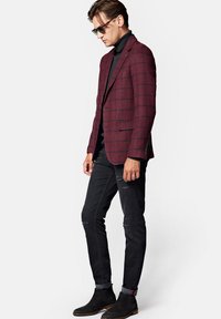 Burgundowa marynarka w kratę z ostrymi klapami na czarnym golfie, zestawiona z podartymi czarnymi dżinsami i czarnymi zamszowymi botkami typu chelsea.