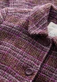 Giacca di lana con un motivo a quadri rosa e marrone, con una superficie testurizzata, bottoni viola e un'etichetta con il nome del marchio.