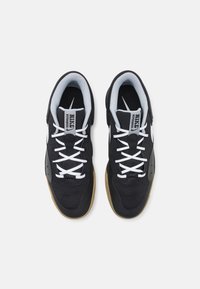 Sorte atletiske sneakers med hvide snørebånd, mesh-overdel og gummisål. Har et diskret brandmærke og kontrasterende lysegrå foring.