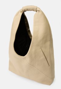 Beige leather hobo bag with a large curved opening, a textured surface, and a streamlined shape. Features a black interior and a side zipper.