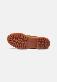 Hnedá gumová podrážka s hlbokými vzormi a vzorom trojlístka, s logom Timberland, prezentujúca trvácnosť a priľnavosť.