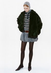 Zwarte faux fur jas, gestreept shirt, denim rok, zwarte visnetkousen en donkere hakken. Bevat een patroon hoofddoek.