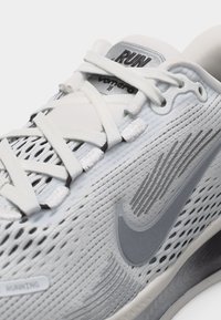 Κοντινό πλάνο λευκού παπουτσιού τρεξίματος Nike με σχεδιασμό από δίχτυ, γκρι λογότυπο σβούρας και κείμενο "RUN" στη γλώσσα που δείχνει τις λεπτομέρειες του κορδονιού.