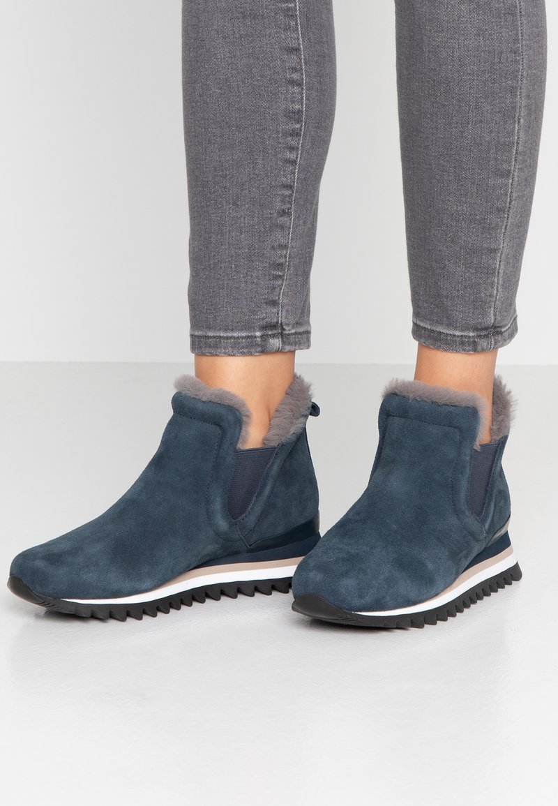 Bottines en daim bleu marine avec doublure en fausse fourrure, panneaux latéraux élastiques et semelles en caoutchouc noir texturé avec une bande blanche au milieu.