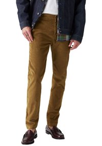 Pantaloni in velluto a coste marroni con vestibilità slim e superficie testurizzata, abbinati a mocassini scuri e una giacca di jeans sopra una camicia a quadri.