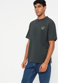 Katoenen T-shirt in donkergrijs met korte mouwen, voorzien van een klein limoengroen logo op de linkerborst en een rechte pasvorm. Geschikt voor casual kleding.