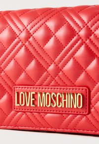 Κόκκινο πορτοφόλι από συνθετικό δερμάτινο υλικό με κεντημένα ρόμβους, με πλακέτα λογότυπου "LOVE MOSCHINO" σε χρυσό. Επιφάνεια με υφή διακοσμημένη με μοτίβο διαμαντιών και ραμμένα διακοσμητικά στοιχεία.