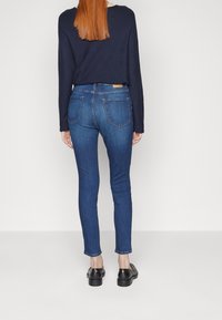 Jeans in denim blu slim fit con vita media, tasche posteriori e un'etichetta in vita. Abbinati a mocassini neri e un top blu navy.