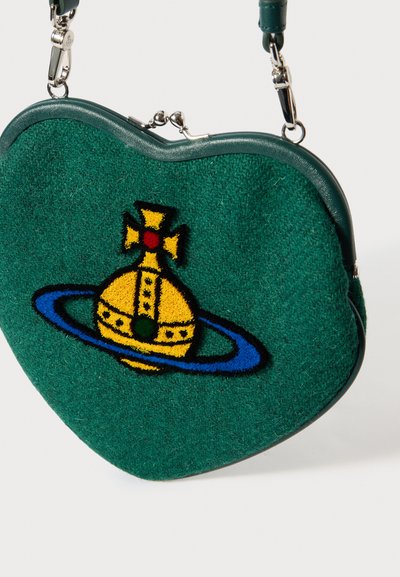 Zaļas krāsas somiņa sirds formas, izgatavota no teksturēta materiāla ar izšuvumu, kurā attēlota dzeltena kroņa un zilas gredzena akcenti. Sudraba detaļas.