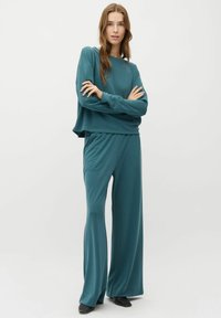Teal lounge set met een cropped lange mouw top en wijde broek. Gladde textuur, ontspannen pasvorm en subtiele naaddetails.